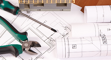 Electrical drawings or diagrams, work tools and house under construction lying on desk, building home concept