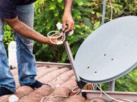 Worker installing satellite dish and antenna on roof top